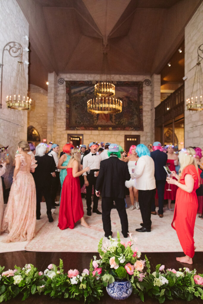 Guests standing on the dance floor wearing hats, wigs, light up sunglasses and flower crowns.