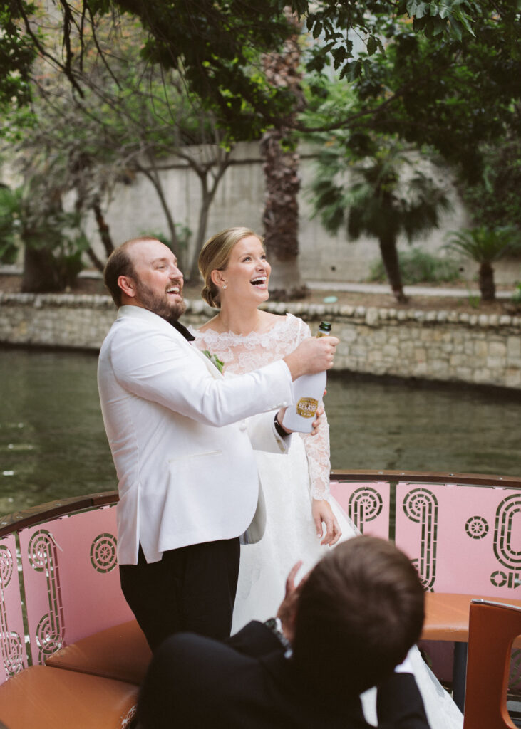 Newlyweds popping a bottle of champagne while cruising down the San Antonio Riverwalk on a river barge