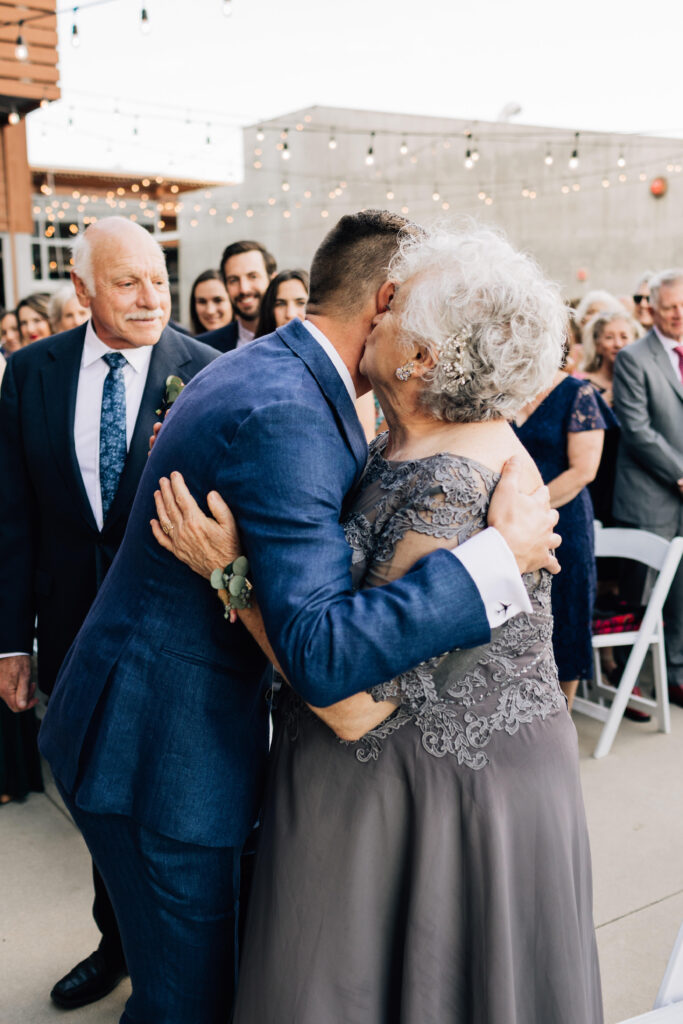 Groom's mom kisses him on the cheek before being seated for the ceremony