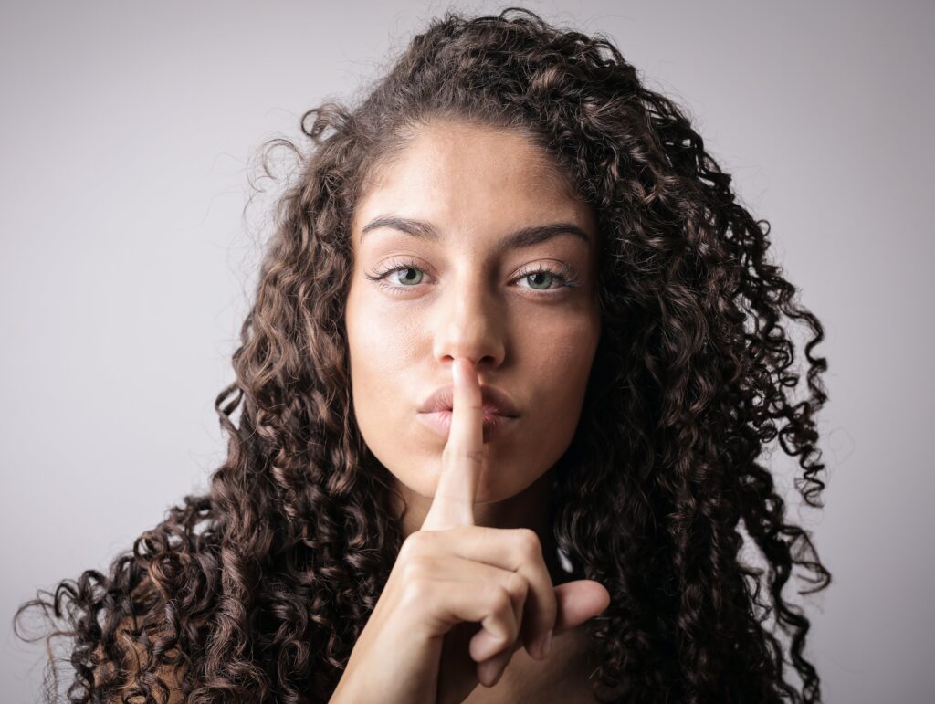 Women with her index finger to her lips saying, "Shh!".