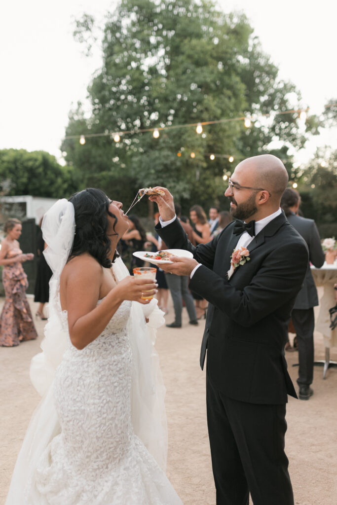 Groom feeding the bride a bite of pizza, debunking the wedding planning myth that you have to please everyone when planning your wedding.